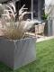 Stilvolle Gartengestaltung mit großem, grauem Pflanzkübel mit Gräsern, daneben eine Terrasse mit Rattan-Gartenmöbeln
