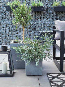 Stilvolle Gartengestaltung mit großem, grauem Pflanzkübel mit Gräsern, daneben eine Terrasse mit Rattan-Gartenmöbeln