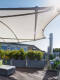 Moderne Dachterrasse mit beigem Sonnensegel, Holzdielenboden, Lounge-Möbeln und bepflanzten rechteckigen Pflanzkübeln an einem sonnigen Tag