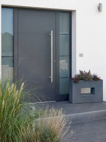 Eingangsbereich mit moderner, dunkelgrauer Haustür und Fenster, stilvoll ergänzt durch einen grauen Pflanzkübel mit dekorativer Bepflanzung mit Gräsern