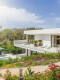 Moderne Luxusvilla mit weißer Fassade und großzügiger Terrasse, umgeben von einem farbenfrohen Garten mit Blick auf eine grüne Landschaft
