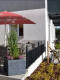 Terrasse eines modernen Cafés mit lava anthraziten Pflanzkübel, lebendigen Pflanzen und rotem Sonnenschirm