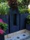 Gartenbereich mit lava dunkelblauen, modernen Pflanzkübeln mit strukturierten Aussparungen, bepflanzt mit Gräsern und Hydrangea
