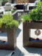 Terrassendekoration mit rostfarbenen Pflanzgefäßen mit Gräsern und Kräutern, dekorativer Windspielkugel und gemütlichen Rattanmöbeln
