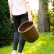 Frau läuft und hält einen leichten rostfarbenen Pflanzkübel rund im Garten